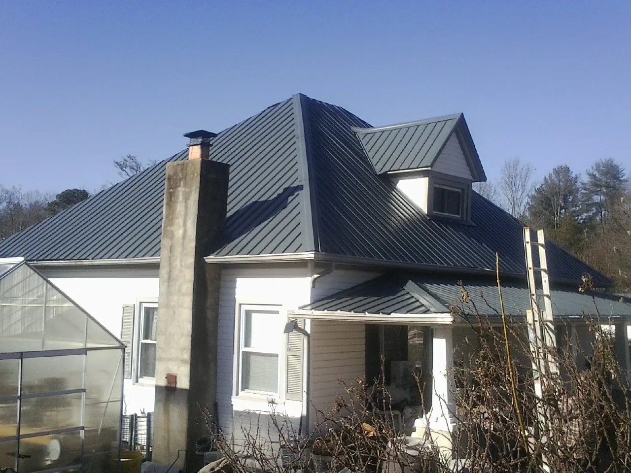 Dark blue standing seam metal roof on a white farmhouse with dormer — Slate & Tile Roof Repair by Roofing Brothers in Pearsall