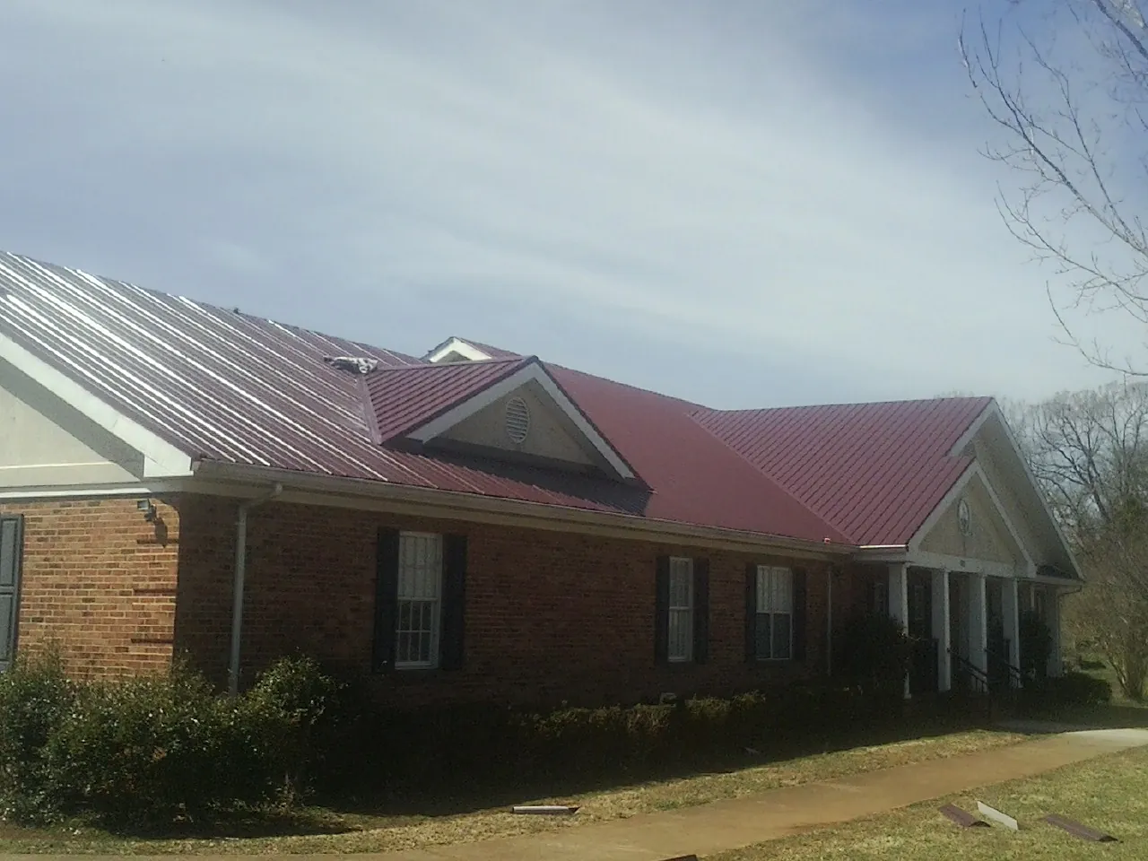 Red metal roof with gabled entries on a long brick building, from a Hail Damage Roof Repair job in Pearsall