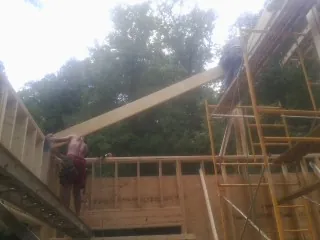 Carpenter raising a rafter beam on a new second story frame in Pearsall