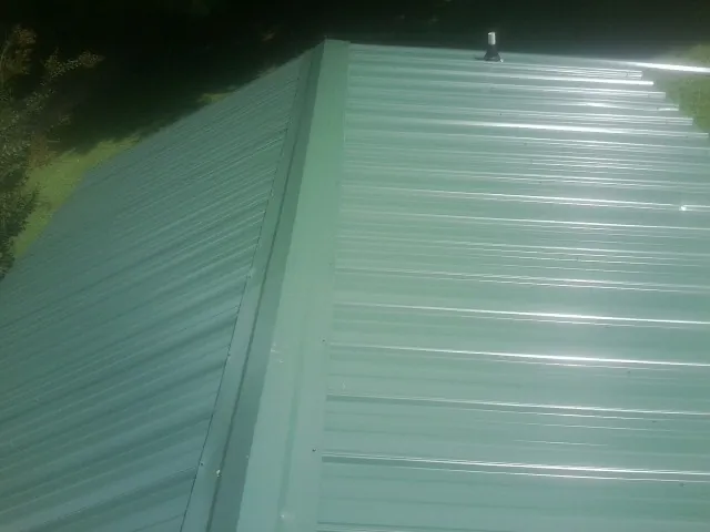 New green metal panels meeting at the ridge of a roof — Flat Roof Repair work by our crew in Pearsall