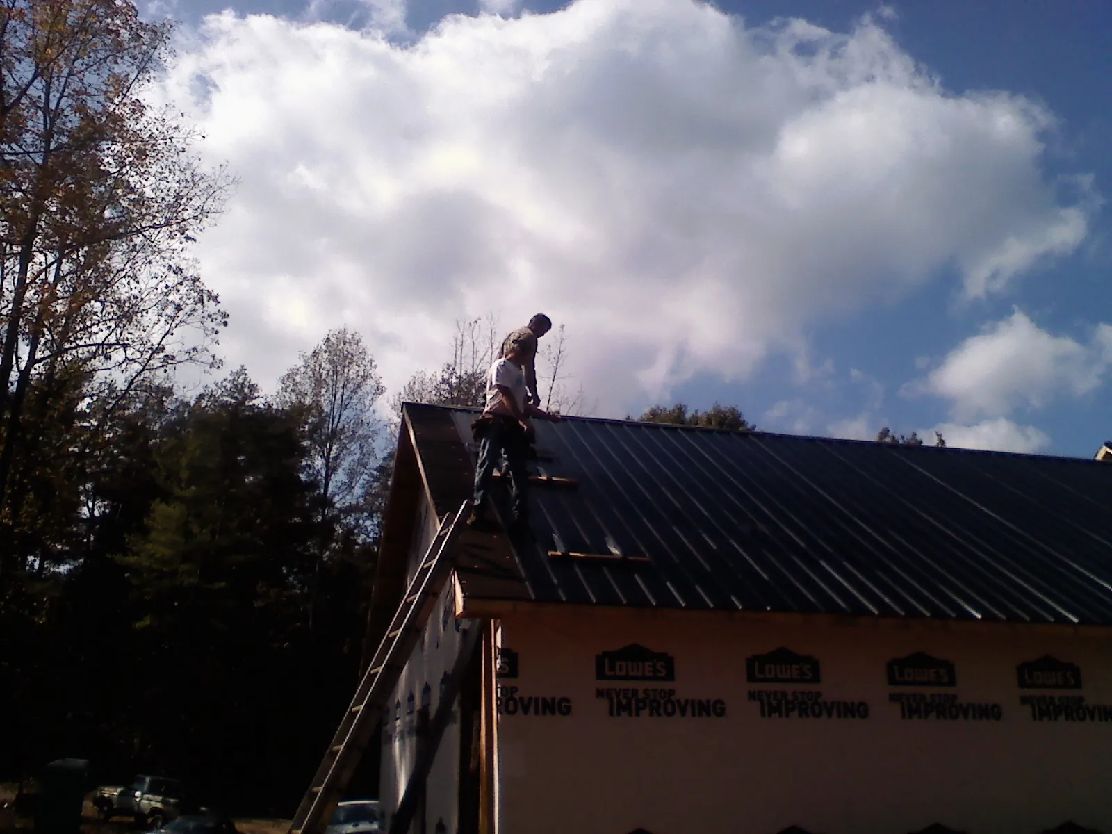 Roofer fastening dark metal panels high against a cloudy sky, from a Roof Inspection job in Pearsall