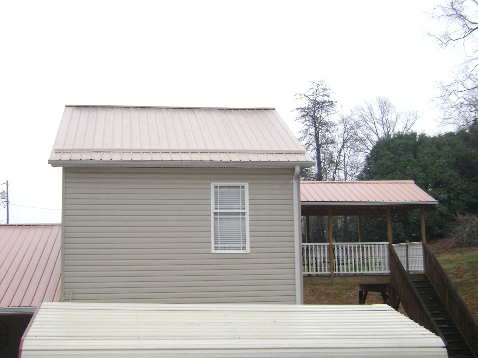 Tan metal roofs on a two story addition and attached porch, from a Roof Replacement job in Pearsall